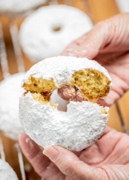 Two hands breaking a powdered sugar donut in half.