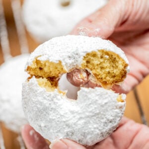 Two hands breaking a powdered sugar donut in half.