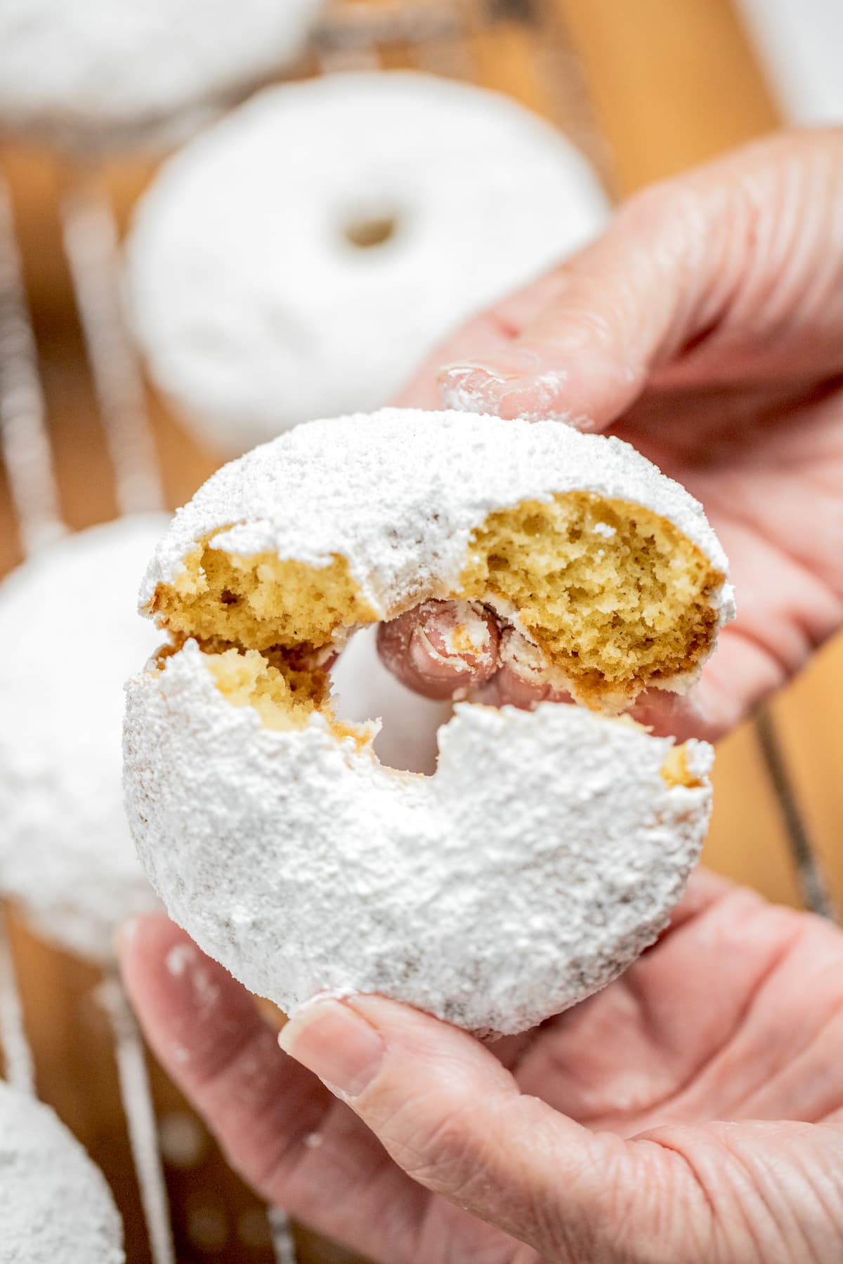 Two hands breaking a powdered sugar donut in half.