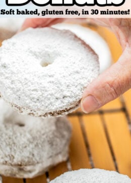 Pinterest pin with a hand holding a powdered sugar donut over a cooling rack.