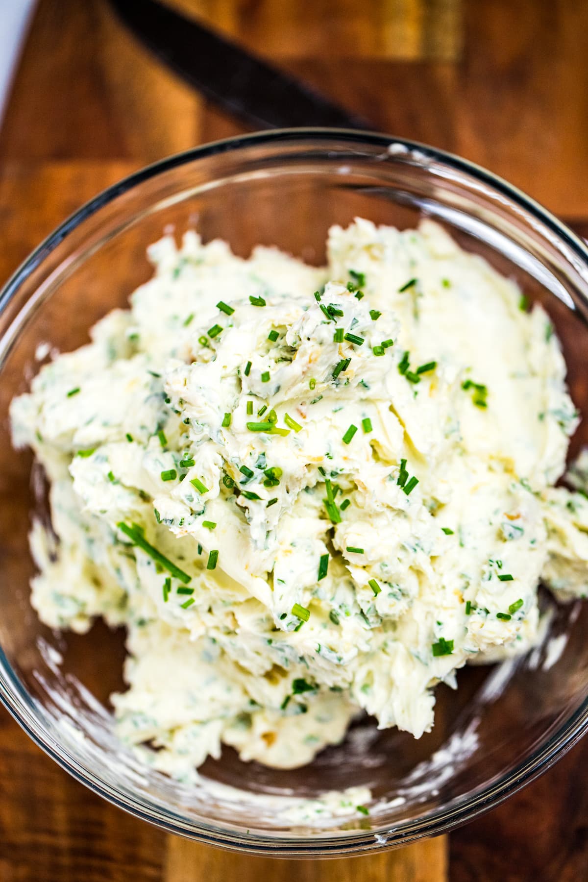 Herb butter in a clear glass bowl on a wooden cutting board.