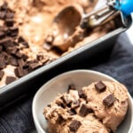 A bowl if chocolate ice cream topped with chocolate chunks next to a bread pan of ice cream with an ice cream scoop.