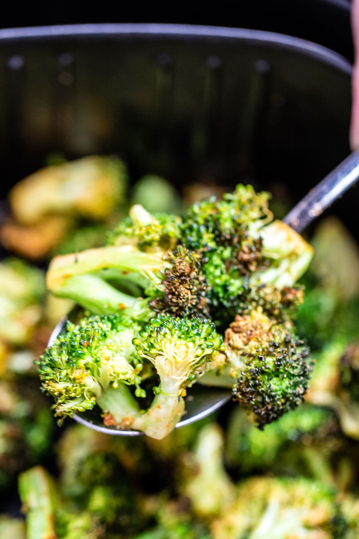 A spoon lifting broccoli out of an air fryer basket.