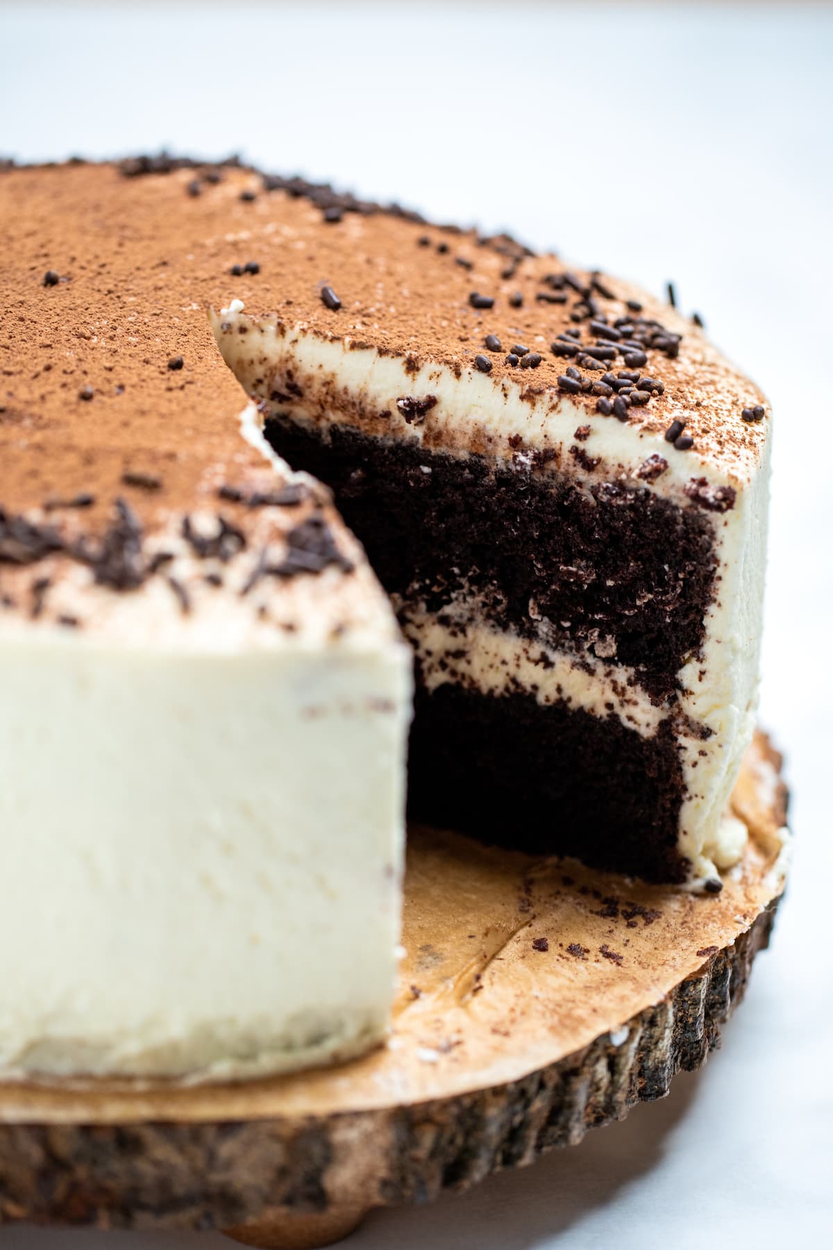 Chocolate coffee cake with a slice missing. The cake is coated in mascarpone frosting, with a middle layer of frosting, and decorated with chocolate sprinkles and a dusting of cocoa powder.