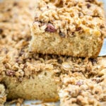 A piece of gluten free coffee cake sitting on top of the baking dish full of coffee cake. There is one piece missing in the dish.