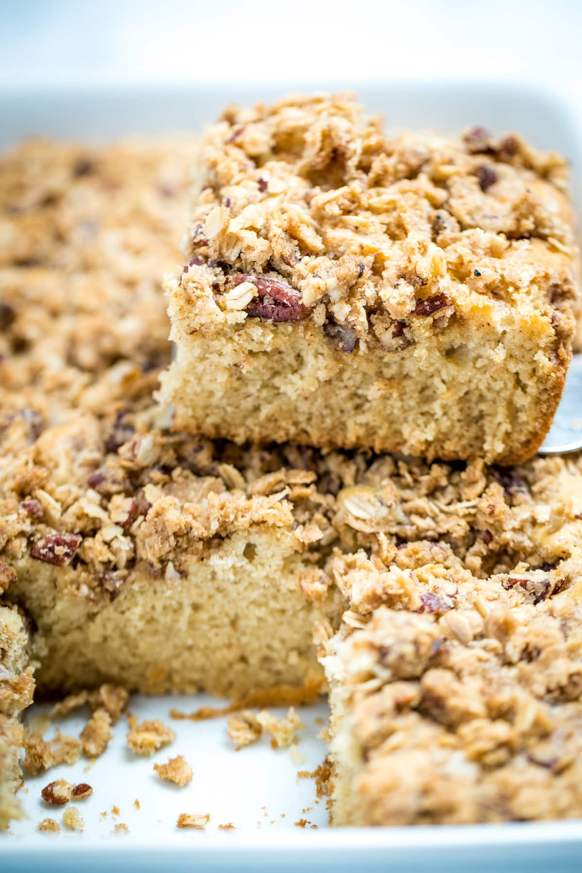 A piece of gluten free coffee cake sitting on top of the baking dish full of coffee cake. There is one piece missing in the dish.