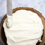 A chocolate cake topped with mascarpone frosting and a frosting spatula.