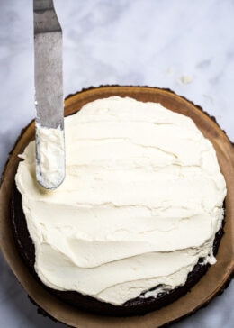 A chocolate cake topped with mascarpone frosting and a frosting spatula.