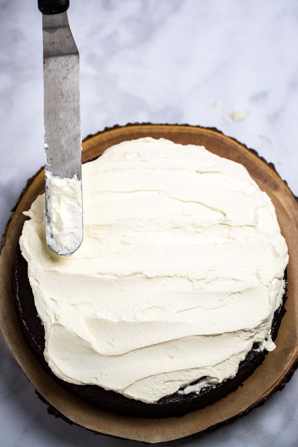 A chocolate cake topped with mascarpone frosting and a frosting spatula.