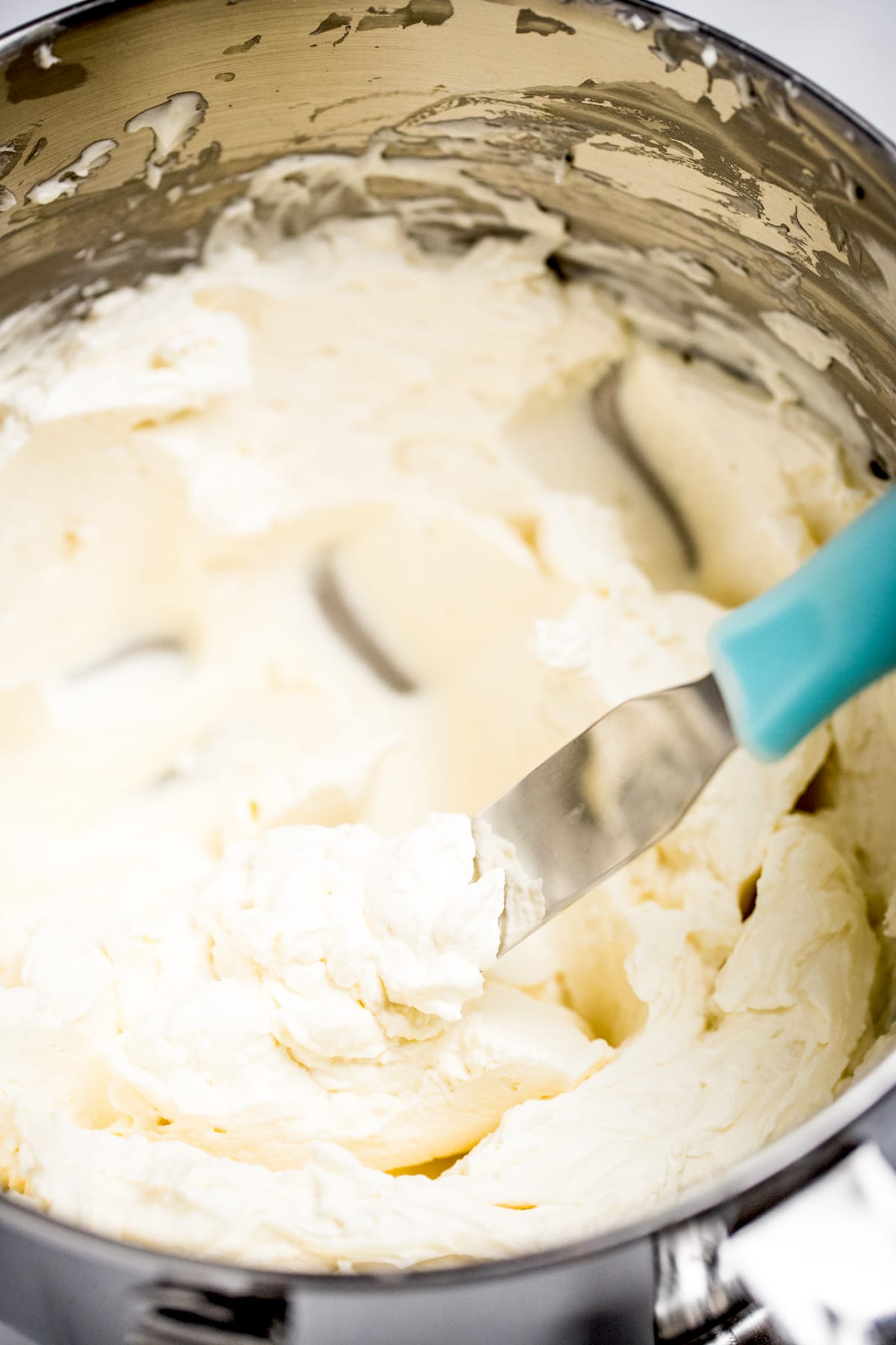 A mixing bowl full of mascarpone frosting with a spatula.