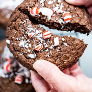 Two hands breaking a peppermint chocolate cookie in half.