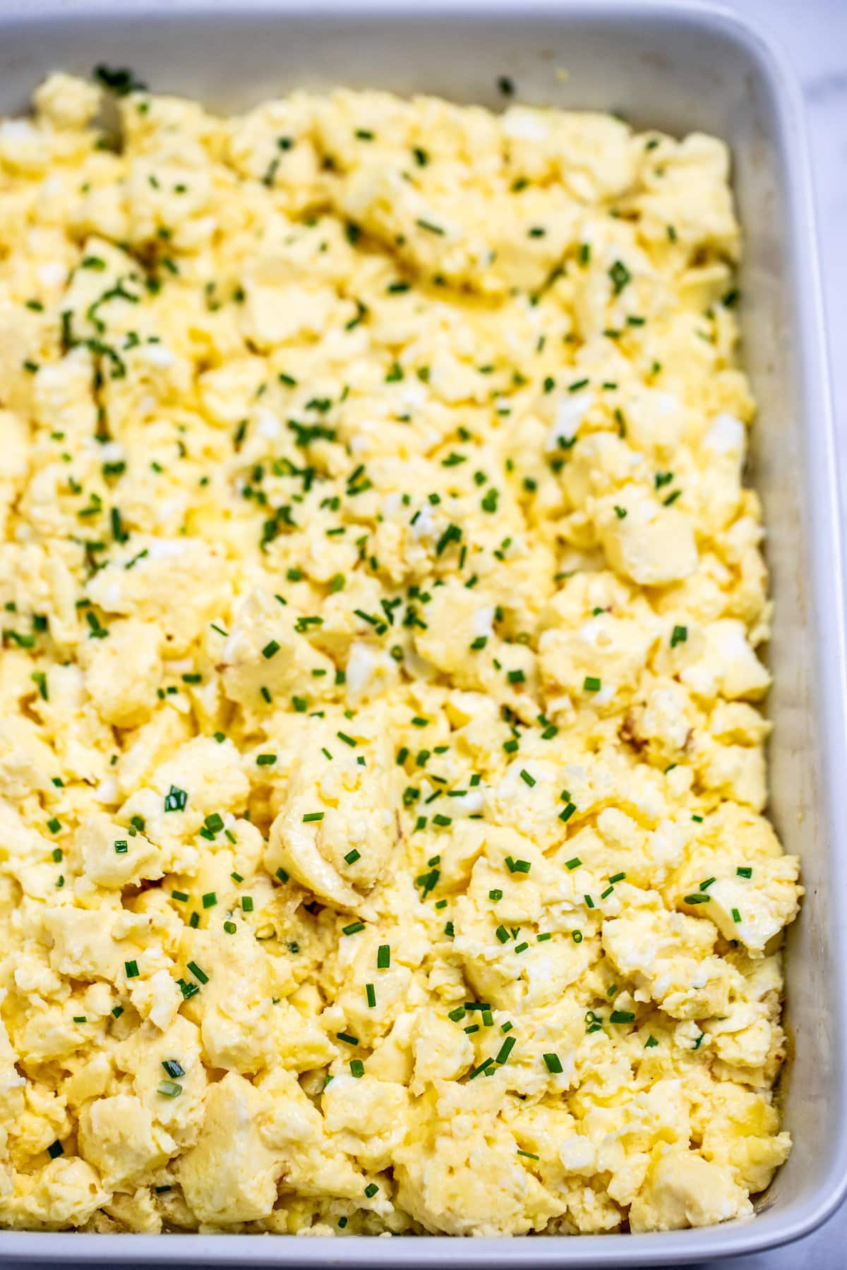 Baking dish full of scrambled eggs with chives on top.