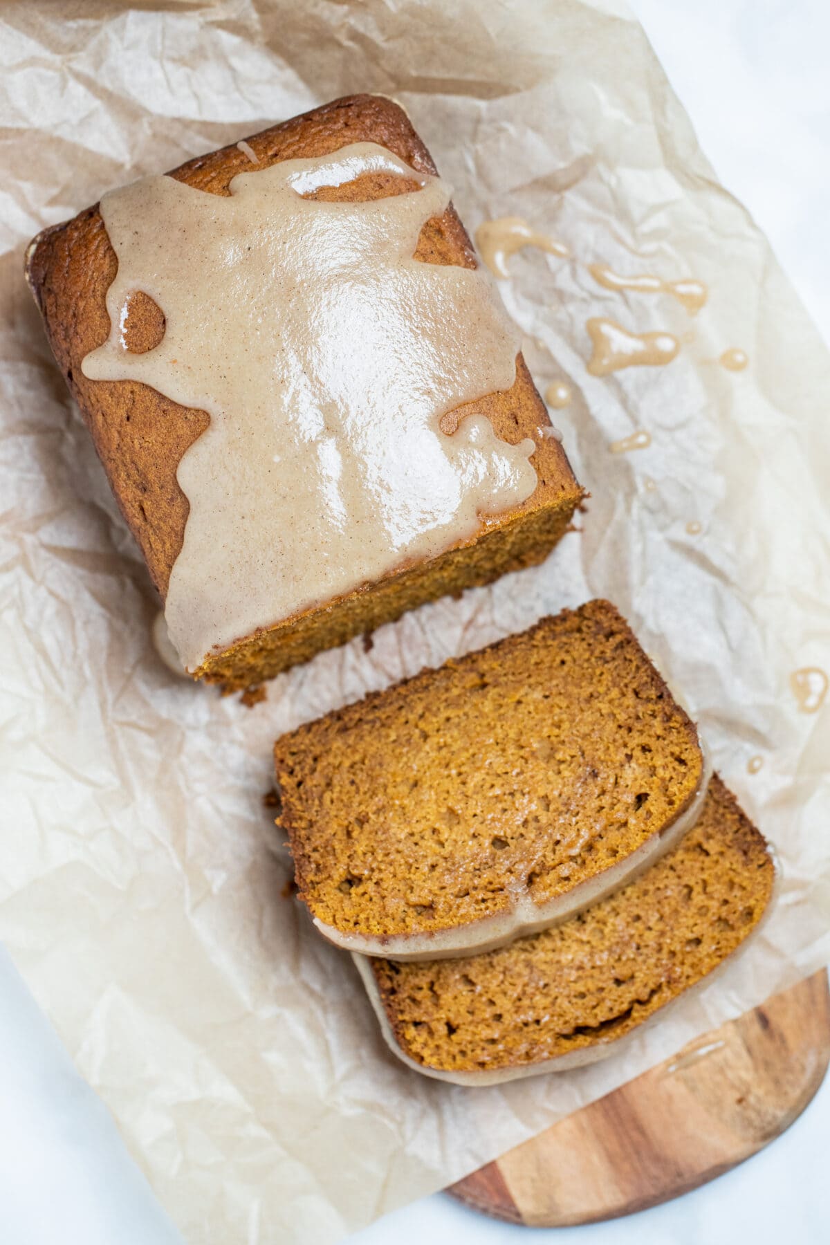 A loaf of gluten free pumpkin bread on a piece of parchment paper with two slices in front of it.