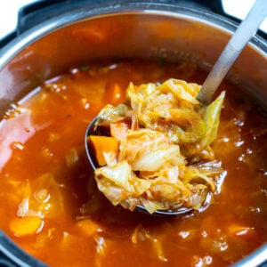 A ladle scooping instant pot cabbage soup out of the instant pot.