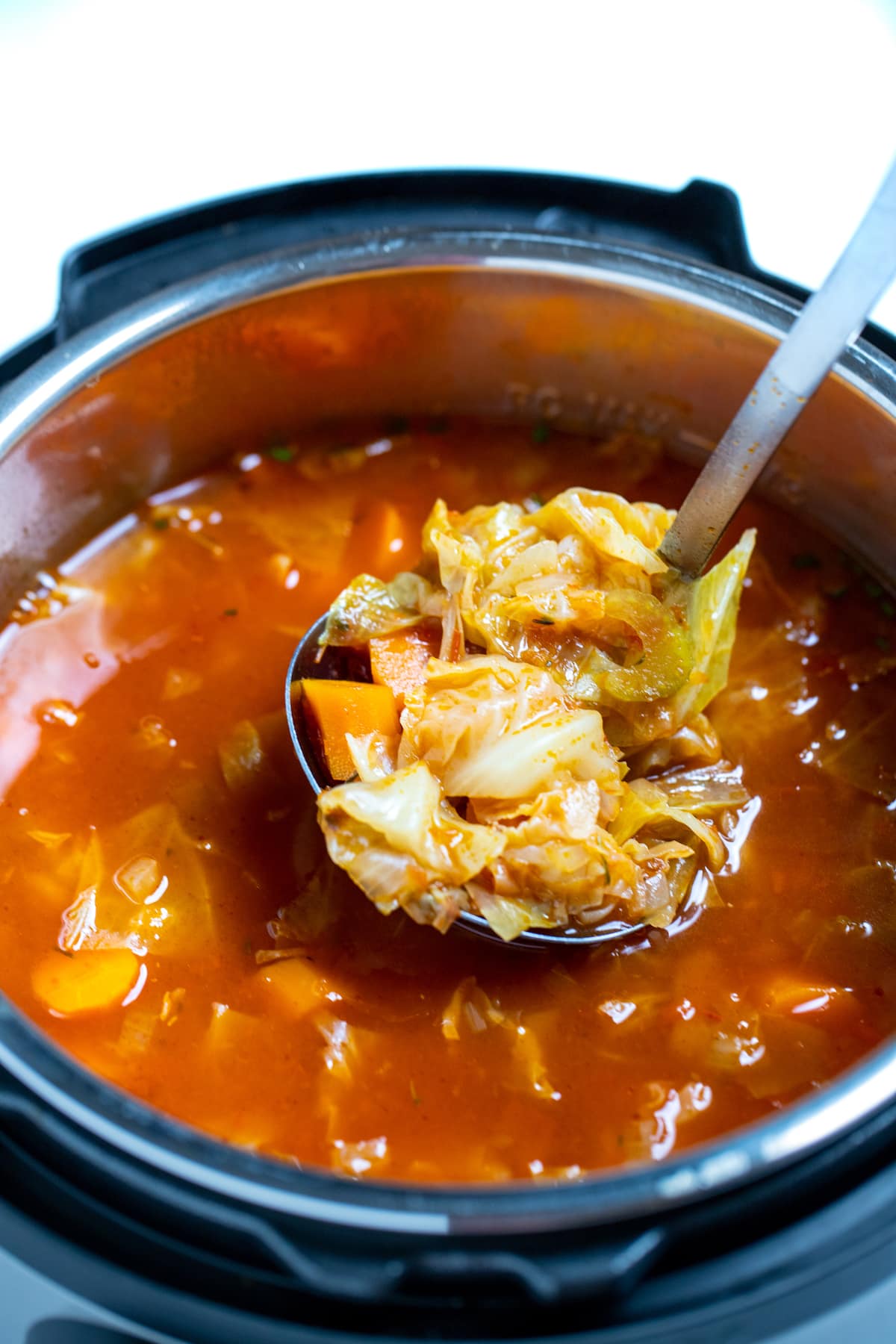 A ladle scooping instant pot cabbage soup out of the instant pot.