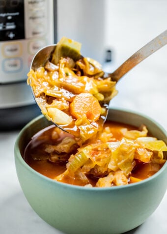 A ladle scooping instant pot cabbage soup into a bowl.