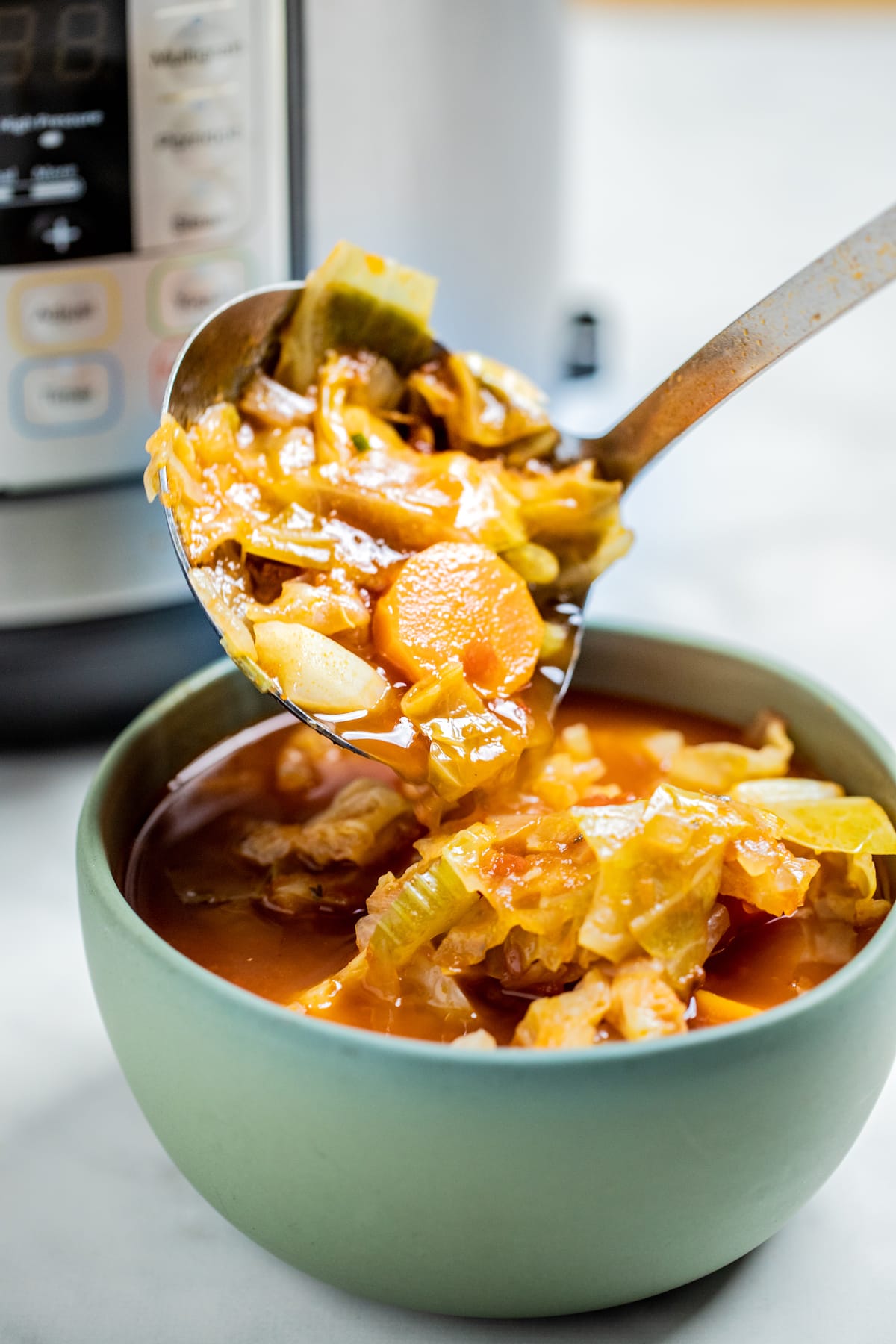 A ladle scooping instant pot cabbage soup into a bowl.