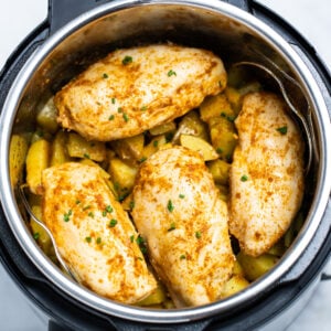 Seasoned chicken breast on top of cubed potatoes in an instant pot.