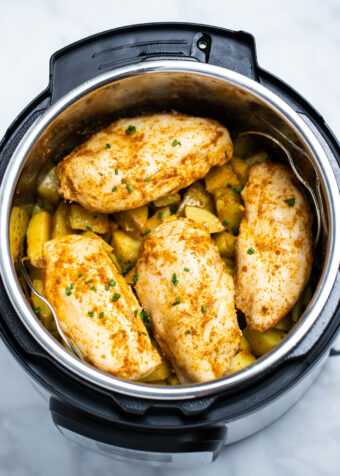 Seasoned chicken breast on top of cubed potatoes in an instant pot.