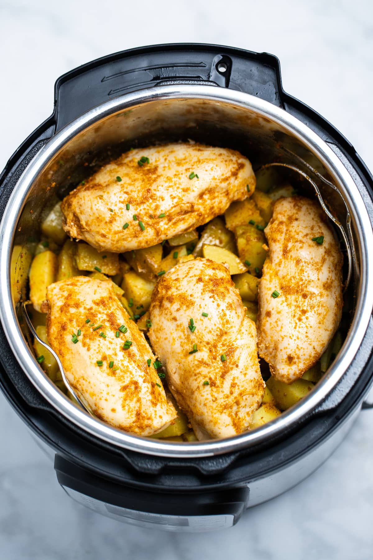 Seasoned chicken breast on top of cubed potatoes in an instant pot.