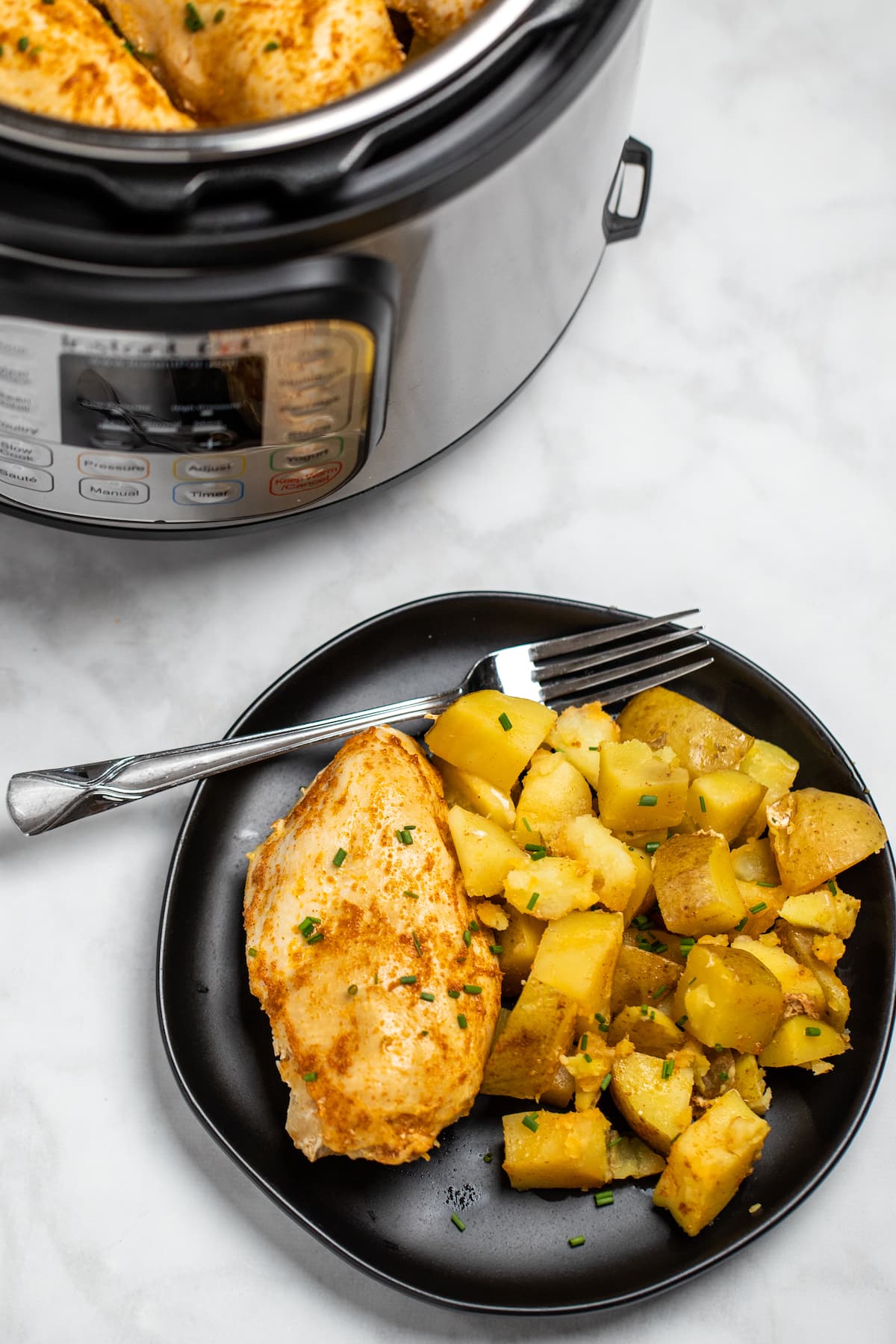 A plate with chicken and potatoes in front of an instant pot.