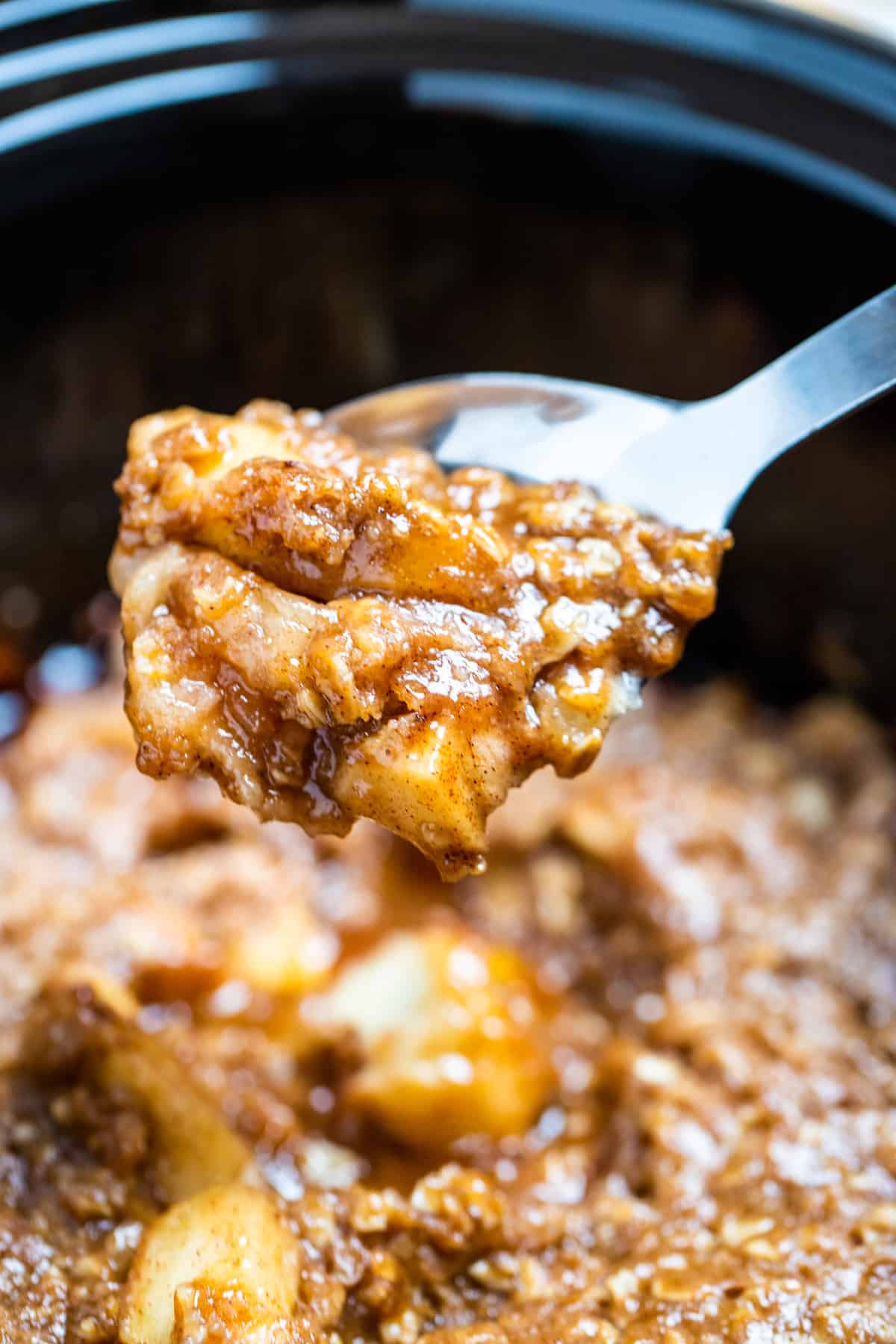 Apple crisp being scooped out of a slow cooker with a spoon.