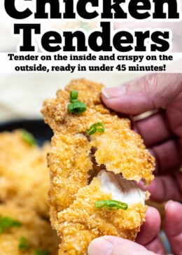 Pinterest pin with hands pulling apart a chicken tender revealing the juicy meat on the inside, and the crispy coating on the outside, with a plate of chicken tenders in the background.