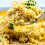 A spoon scooping broccoli mac and cheese out of a baking dish.