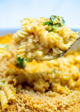 A spoon scooping broccoli mac and cheese out of a baking dish.