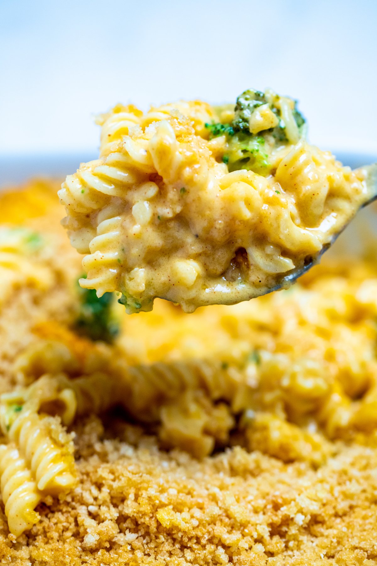 A spoon scooping broccoli mac and cheese out of a baking dish.