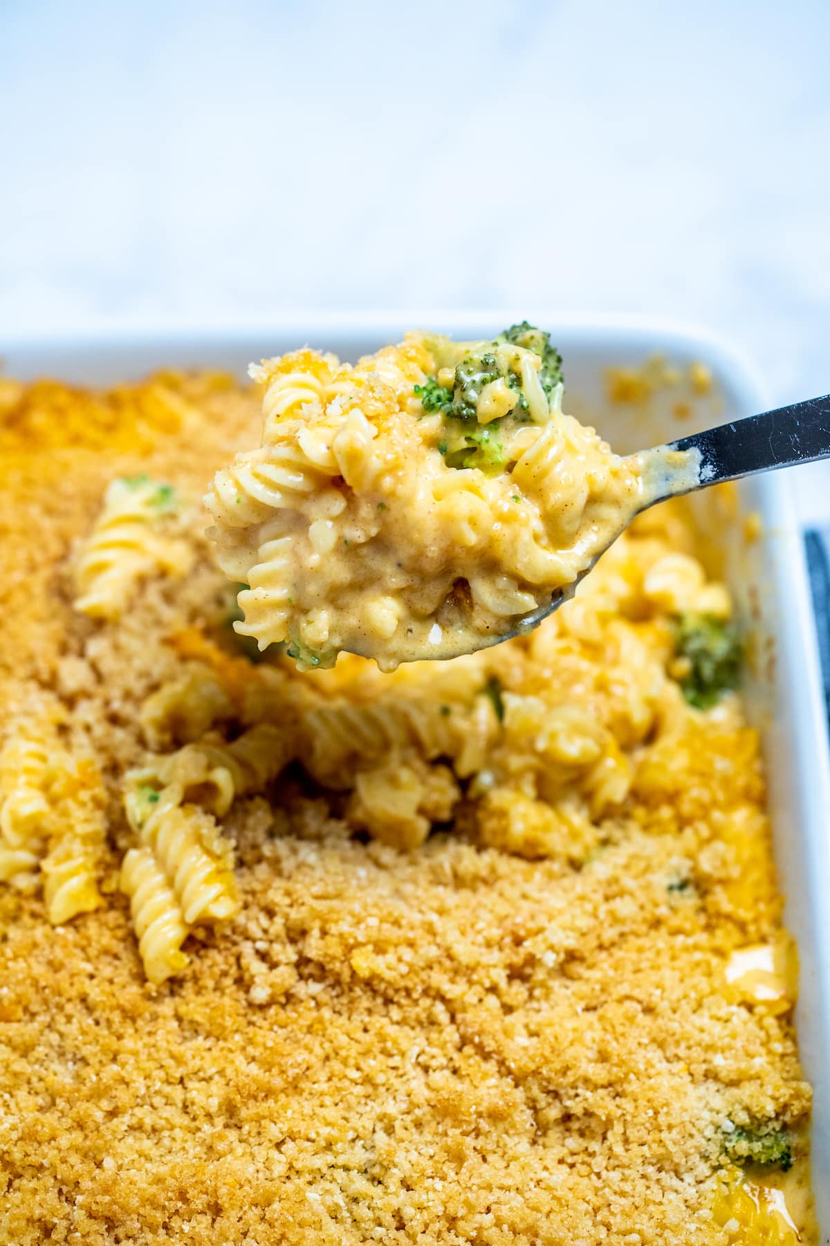 A spoon scooping broccoli mac and cheese out of a baking dish.