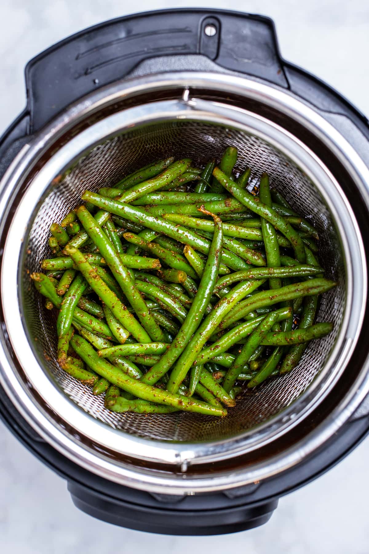 Cooked green beans sitting in an instant pot with a steamer basket.