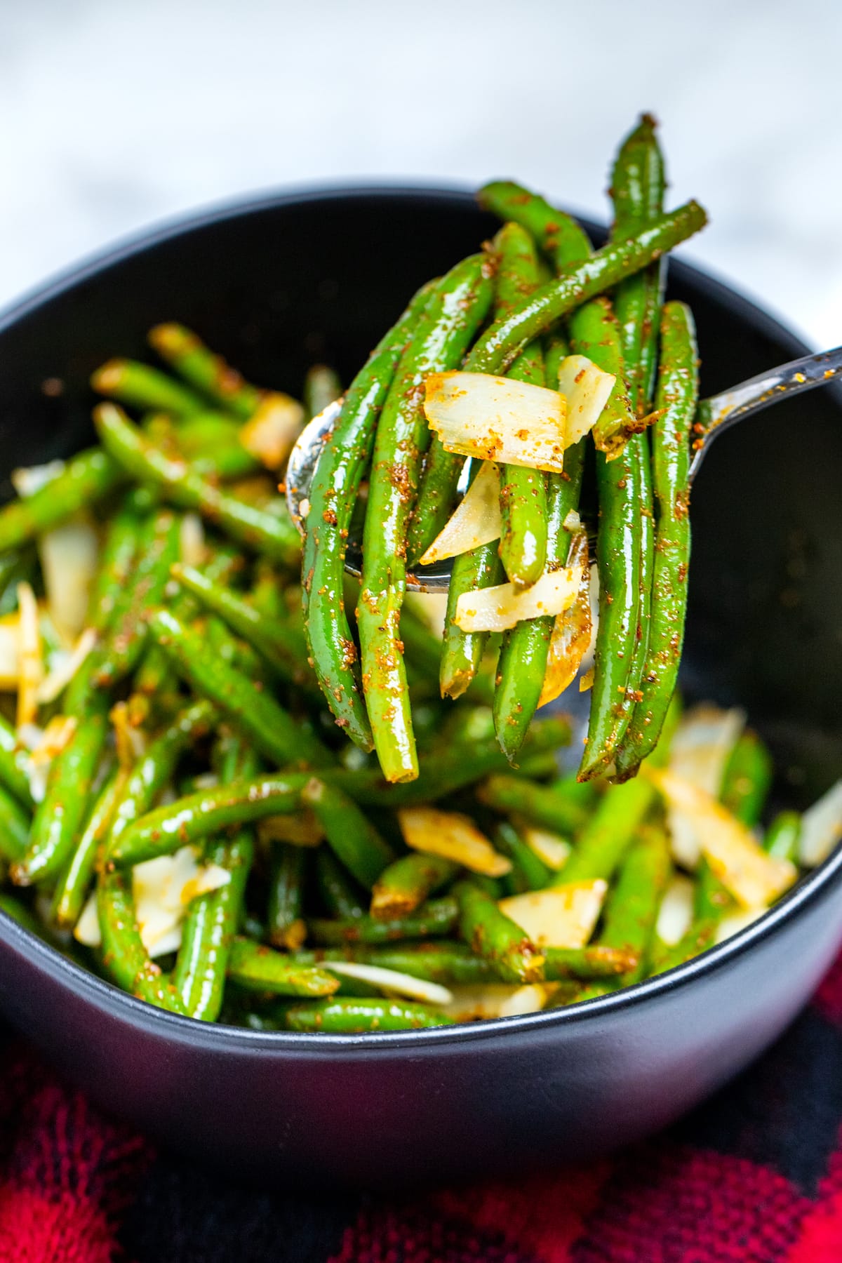 A bowl of instant pot green beans on the table topped with shredded parmesan cheese, and a spoon lifting out a serving of beans.