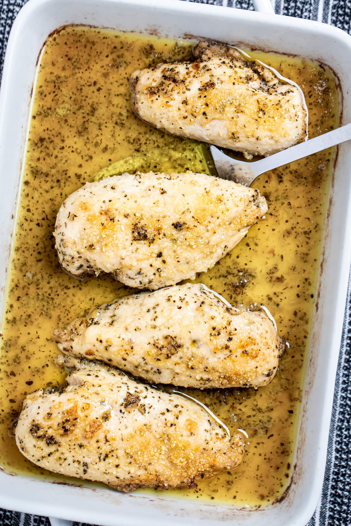 A baking dish of Italian Dressing Chicken and a spatula lifting one piece up.