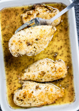 A baking dish of Italian Dressing Chicken and a spatula lifting one piece up.