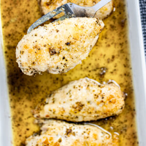 A baking dish of Italian Dressing Chicken and a spatula lifting one piece up.