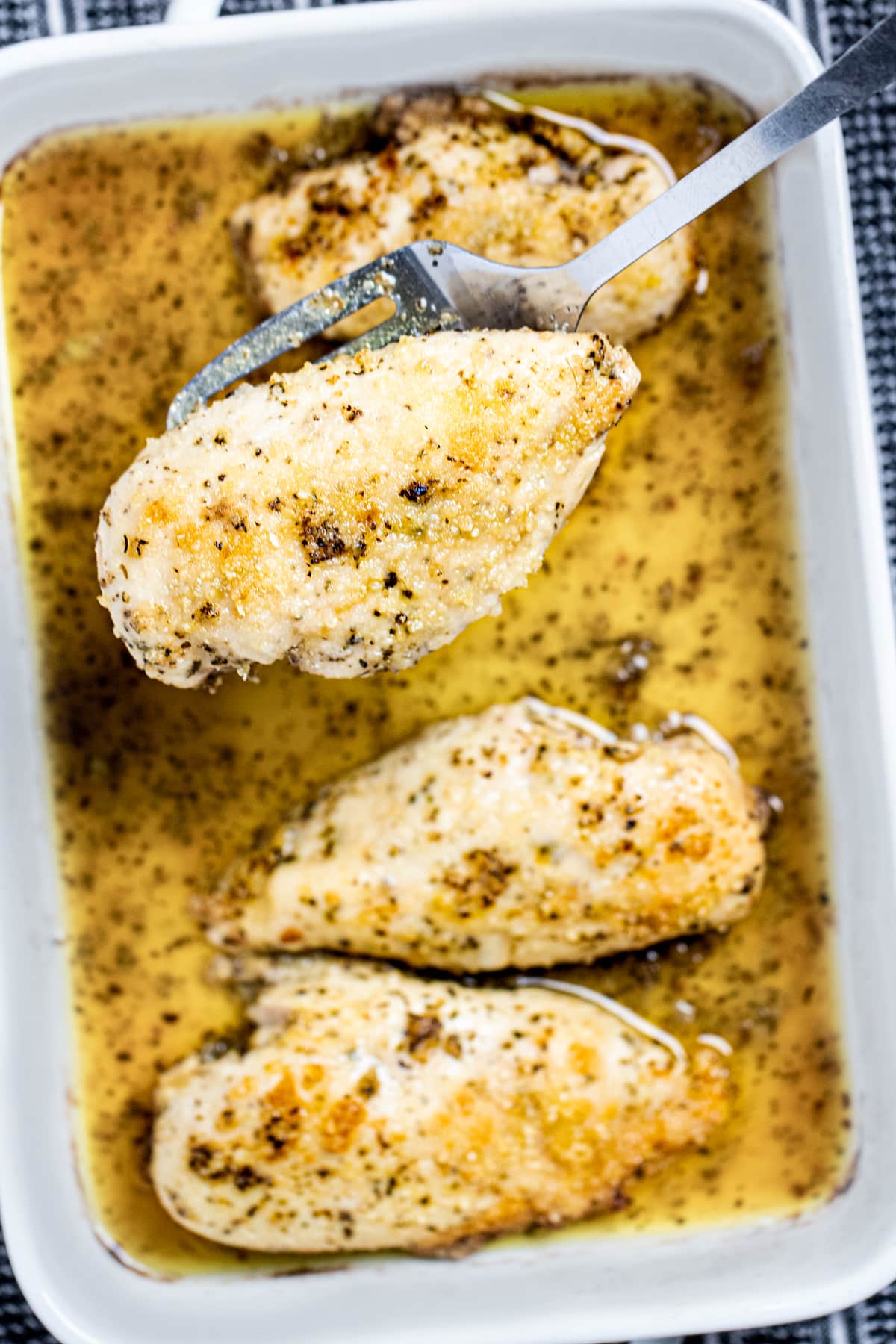 A baking dish of Italian Dressing Chicken and a spatula lifting one piece up.