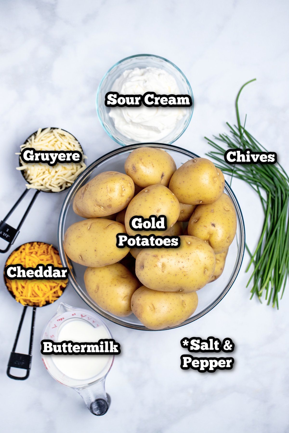 Individual ingredients for cheesy mashed potatoes on a marble table.