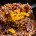 A spoon lifting a portion of crockpot sweet potato casserole out of the slow cooker.