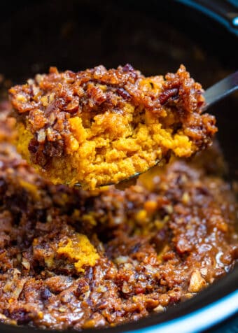 A spoon lifting a portion of crockpot sweet potato casserole out of the slow cooker.