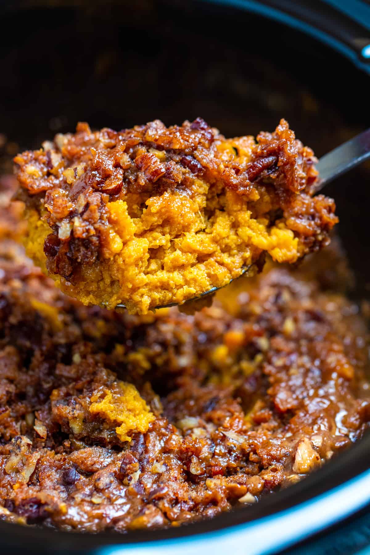 A spoon lifting a portion of crockpot sweet potato casserole out of the slow cooker.