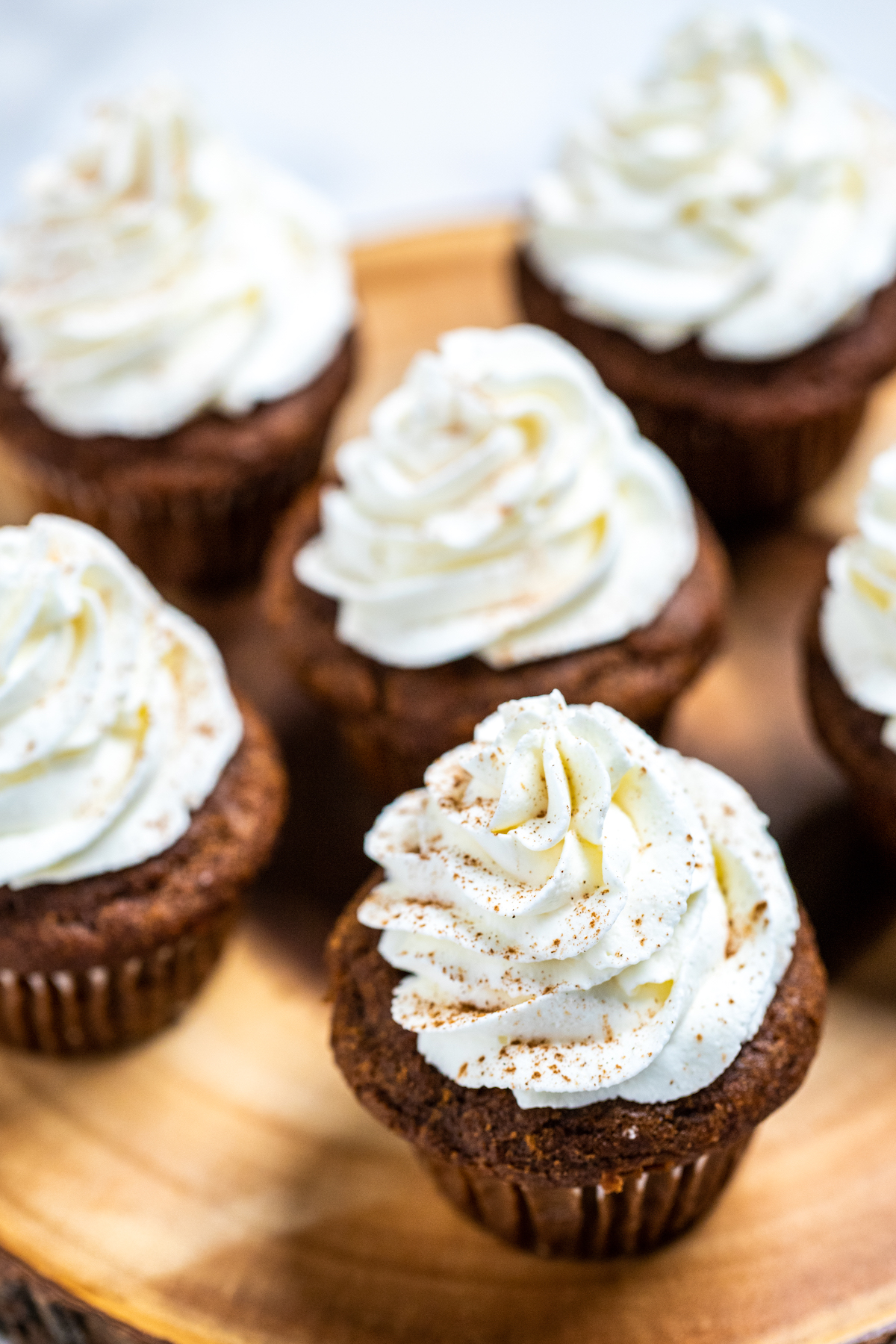 Gingerbread cupcakes topped with a swirl of frosting sitting on top of a wooden board.