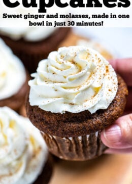 Pinterest pin with a hand holding a gingerbread cupcake topped with frosting above a wooden cutting board and other cupcakes.