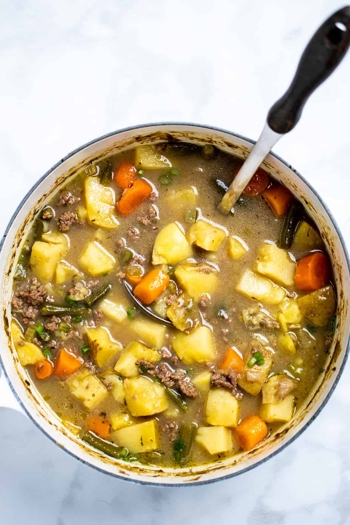 A dutch oven full of ground beef soup with a ladle.