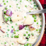 Creamed peas and potatoes in a skillet with a ladle on top of a plaid towel.