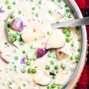 Creamed peas and potatoes in a skillet with a ladle on top of a plaid towel.