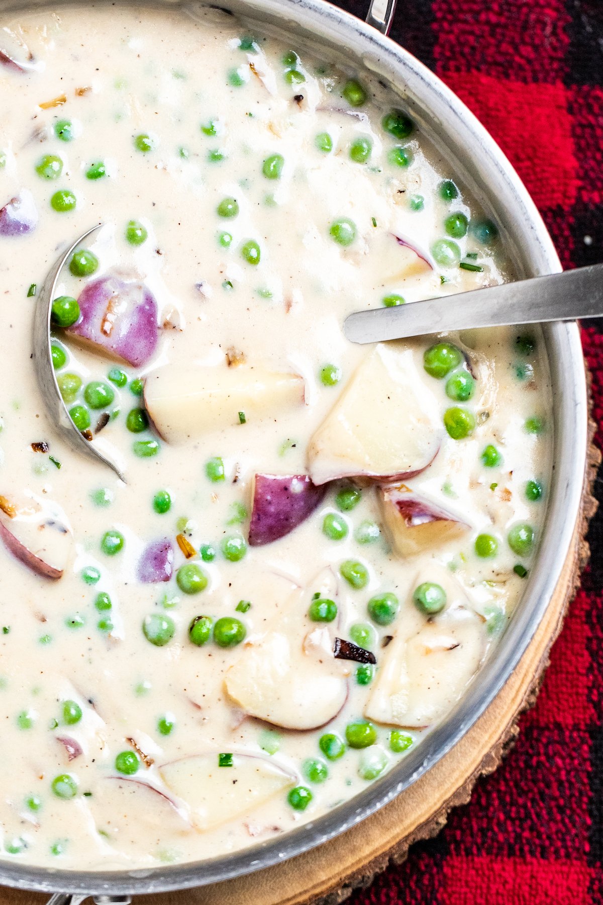 Creamed peas and potatoes in a skillet with a ladle on top of a plaid towel.