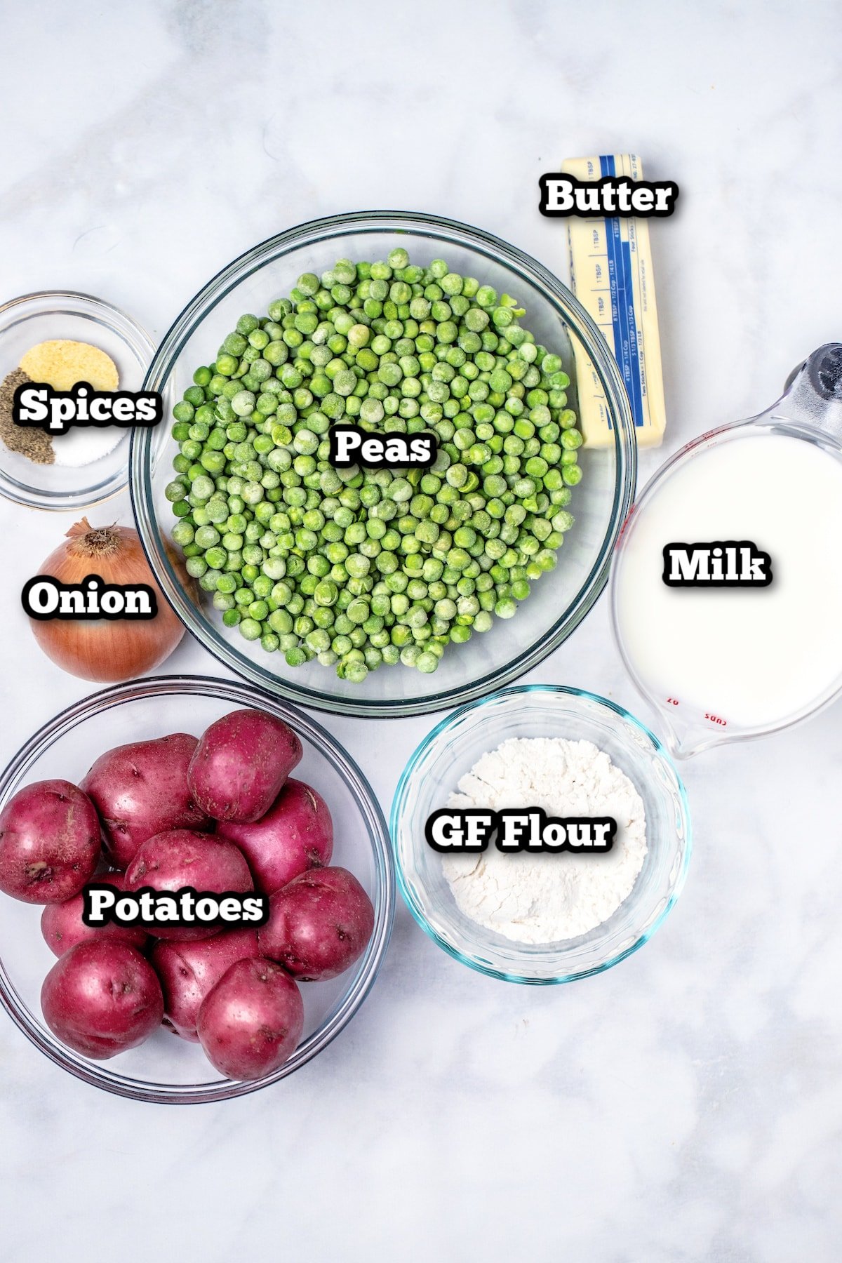 Individual ingredients for creamed peas and potatoes on a marble table.