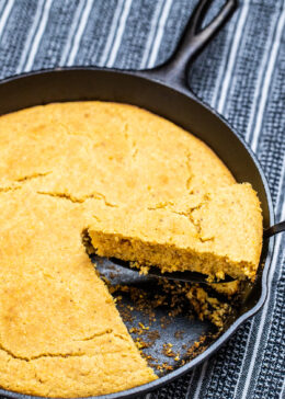 A cast iron skillet of gluten free cornbread with a slice being lifted out.