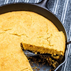 A cast iron skillet of gluten free cornbread with a slice being lifted out.